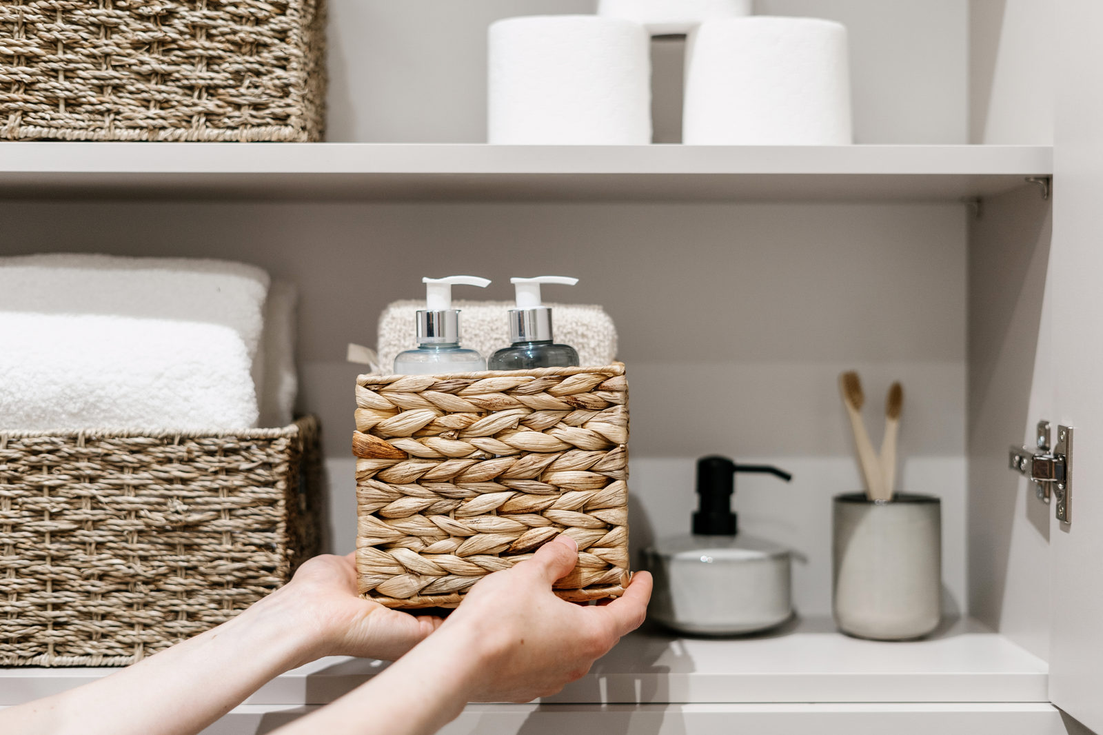 Organization of space in the bathroom cabinet. Cropped view of woman putting wicker box on shelf